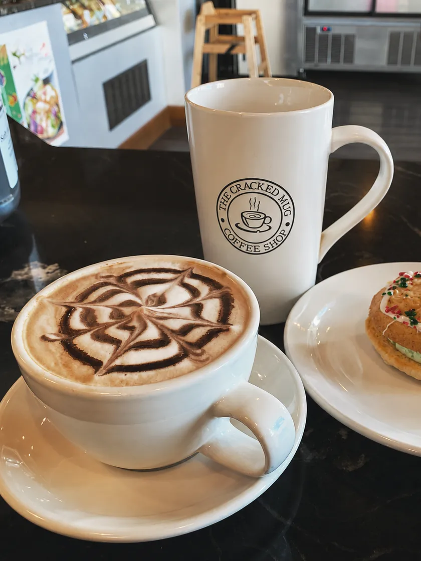 Coffee with latte art beside a Cracked Mug cup