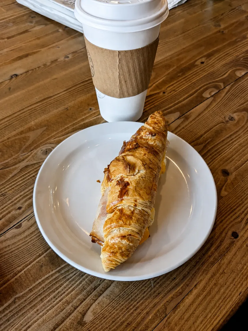 A croissant and takeaway coffee on a wooden table
